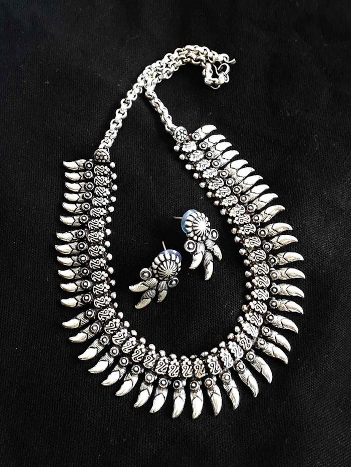 Intricate silver necklace and earrings displayed on a black background.